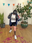 Eine Frau trägt ein Sport-Outfit mit Boxhandschuhen und schlägt mit diesen Richtung Kamera.